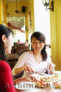 Asia Images Group - Young women at cafe, eating pizza