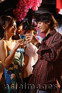 Asia Images Group - Couple standing in club, toasting with drinks, people in the background