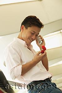 Asia Images Group - Man looking at ring box, using mobile phone, smiling
