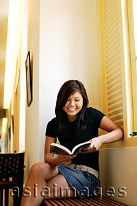 Asia Images Group - Young woman sitting, reading a book, smiling