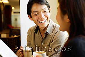 Asia Images Group - Couple sitting, holding coffee cups, smiling at each other