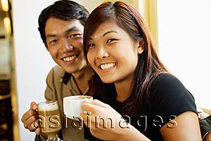 Asia Images Group - Couple sitting, holding coffee cups, smiling at camera
