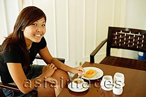 Asia Images Group - Young woman sitting, food and coffee in front of her, looking at camera