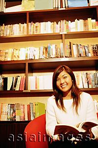 Asia Images Group - Young woman, sitting on chair, holding book, looking at camera