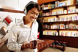 Asia Images Group - Young man listening to music, smiling, looking down at CD