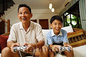 Asia Images Group - Father and son, sitting on sofa, holding video game controllers