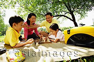Asia Images Group - Family playing chess, sitting on picnic mat