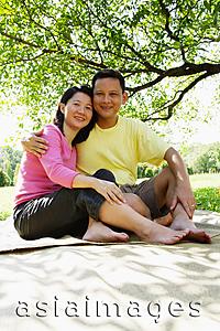 Asia Images Group - Couple sitting on picnic mat, looking at camera