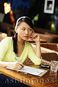 Asia Images Group - Young woman sitting at table with pen and paper, hand on face