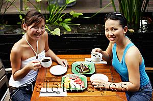 Asia Images Group - Two women sitting at table, having coffee and fruits, looking up at camera