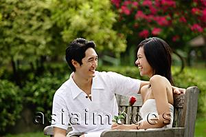 Asia Images Group - Couple sitting on park bench, looking at each other, woman holding rose