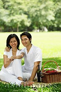 Asia Images Group - Couple sitting with picnic basket, smiling at camera