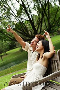 Asia Images Group - Couple sitting on park bench, looking up, man pointing