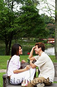Asia Images Group - Couple on park bench, sitting face to face, woman holding a rose