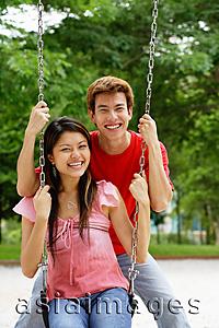 Asia Images Group - Couple in playground, woman sitting on swing, man behind her, looking at camera