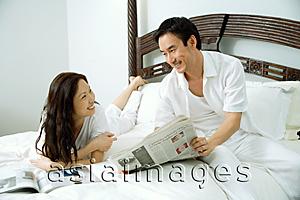 Asia Images Group - Couple in bedroom, man showing woman newspaper