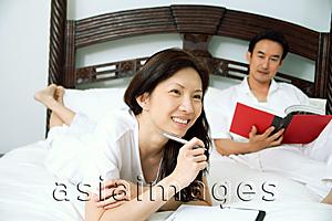 Asia Images Group - Couple in bedroom, woman holding pen, man reading book