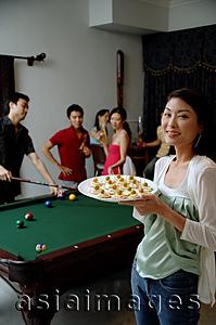 Asia Images Group - Woman with plate of appetizers, smiling at camera, people in the background