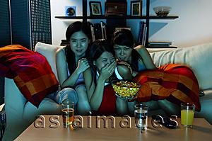 Asia Images Group - Three young women sitting on sofa in living room, watching TV