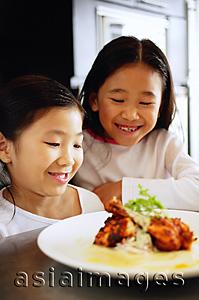 Asia Images Group -  Two girls looking at a plate of food, smiling