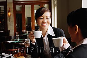 Asia Images Group - Two businesswomen at cafe, holding cups, smiling