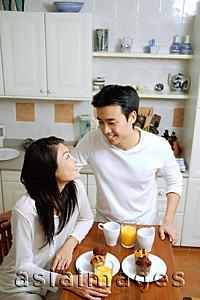 Asia Images Group - Couple having breakfast in kitchen, smiling at each other
