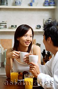 Asia Images Group - Couple in kitchen, having breakfast, both holding mugs