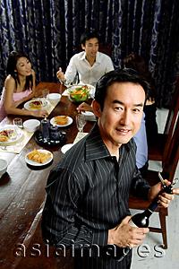 Asia Images Group - Man opening wine bottle, smiling at camera, people in the background