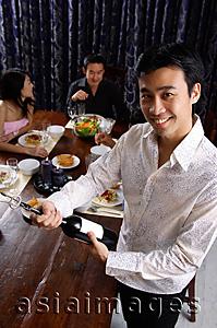 Asia Images Group - Man opening bottle of wine, smiling at camera, people in the background
