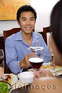 Asia Images Group - Man at dinner table, holding wine glasses, facing another person