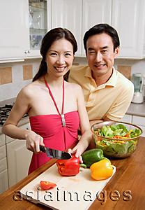 Asia Images Group - Couple in kitchen, woman chopping vegetables, smiling at camera
