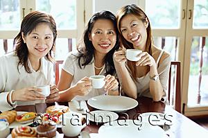 Asia Images Group - Three women sitting side by side in cafe, smiling at camera