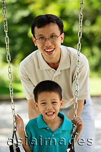 Asia Images Group - Boy on swing, father behind him, both smiling at camera