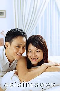 Asia Images Group - Couple lying on bed, looking at camera