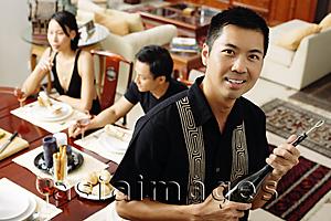 Asia Images Group - Man holding wine bottle, looking at camera, people in the background, sitting around dining table