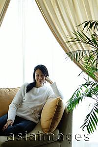 Asia Images Group - Woman in living room, sitting on sofa, looking at camera