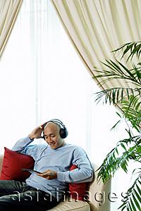 Asia Images Group - Man on sofa with headphones, listening to music