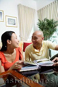 Asia Images Group - Couple at home in living room, photo album in front of them