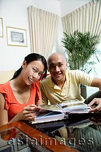 Asia Images Group - Couple at home in living room, photo album in front of them, smiling at camera