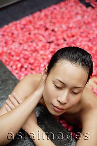 Asia Images Group - Woman leaning on edge of tub filled with floating rose petals, eyes closed