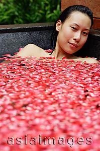 Asia Images Group - Woman in tub filled with floating rose petals, looking at camera