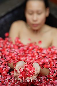 Asia Images Group - Woman in tub holding flower petals in cupped hands, selective focus