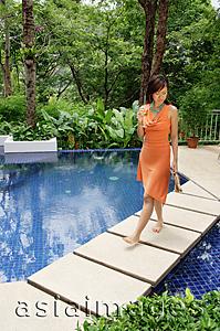 Asia Images Group - Woman walking barefoot by swimming pool, holding glass of champagne and sandals