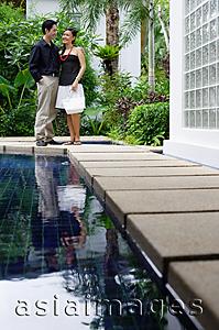 Asia Images Group - Couple standing side by side next to swimming pool