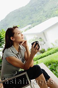 Asia Images Group - Woman sitting, holding coffee mug, hand on chin