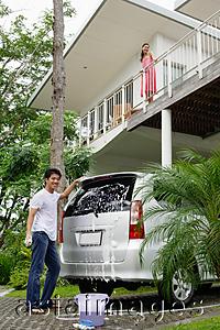Asia Images Group - Man washing car, woman standing on balcony looking down