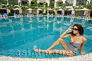 Asia Images Group - Woman in swimwear, sitting next to swimming pool, building in the background