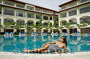 Asia Images Group - Woman lying next to swimming pool, building in the background
