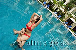 Asia Images Group - Couple in swimming pool, woman sitting on mans shoulders, looking away