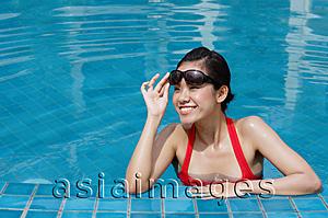 Asia Images Group - Woman leaning on edge of swimming pool, adjusting sunglasses, smiling